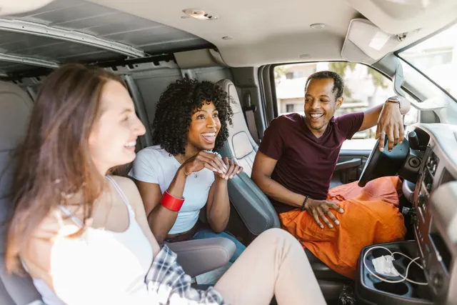Trois passagers rient ensemble à bord d'un minibus, le conducteur se retourne vers eux.
